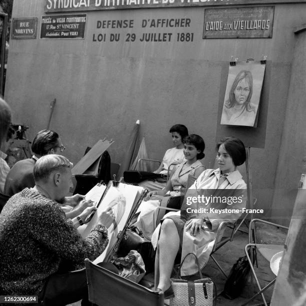 Dans une rue montant au Sacré-Coeur, des femmes posent pour se faire tirer le portrait par des peintres de rue, à Paris, France le 7 août 1964.