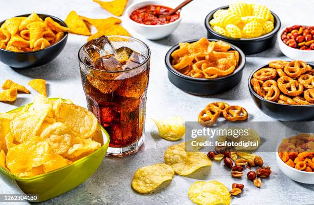 cola soda glas und salzige snacks auf grauen tisch geschossen - chips schüssel stock-fotos und bilder