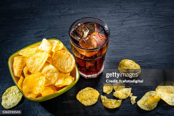 het sodaglas van de cola en aardappelschips in een kom die op zwarte leisteenlijst wordt ontsproten - frisdrank stockfoto's en -beelden