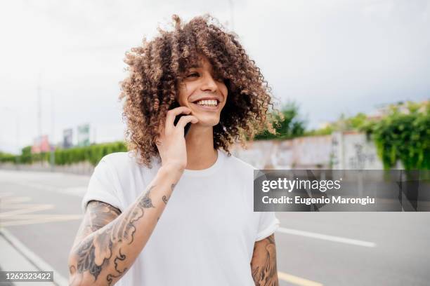 portrait of man with tattooed arms and long brown curly hair, using mobile phone. - curly hair man stock pictures, royalty-free photos & images