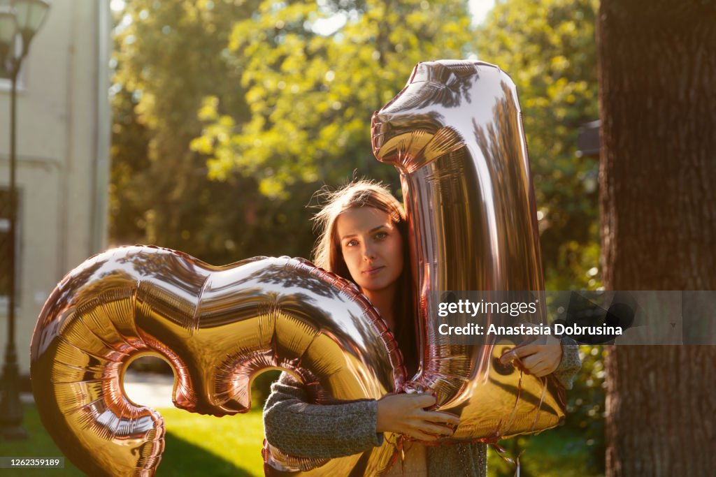 Cheerful woman celebrates a thirty one years birthday with big golden balloons