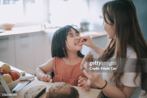an asian chinese mid adult woman enjoying bread making baking time with her 8 years old daughter cutting the loaf of bread - baking bread stock pictures, royalty-free photos & images