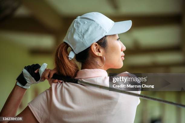 nahaufnahme der asiatischen jungen golferin schwingen ihren fahrer auf golf driving range - golfhandschuh stock-fotos und bilder