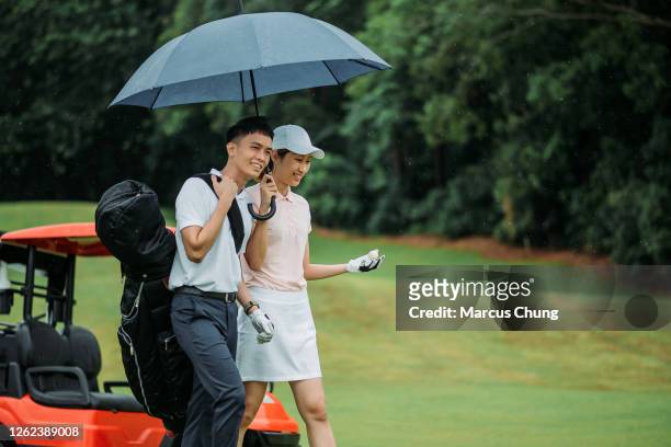 asian chinese young smiling couple golfer with blue umbrella on the golf course - golf driver stock pictures, royalty-free photos & images
