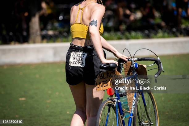 July 25: A protester walking a bicycle has a sign on their back of their shorts that say, "Arrest Killer Cops" and another on the bicycle that says,...