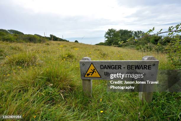 a warning sign on the coast path in devon - jurassic coast world heritage site 個照片及圖片檔