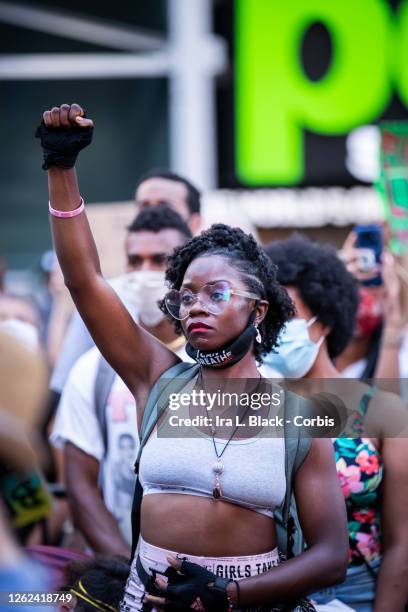 July 26: A protester wearing a mask around their neck that says, "I can't breathe" and a pair of heart shaped glasses holds a raised black power fist...