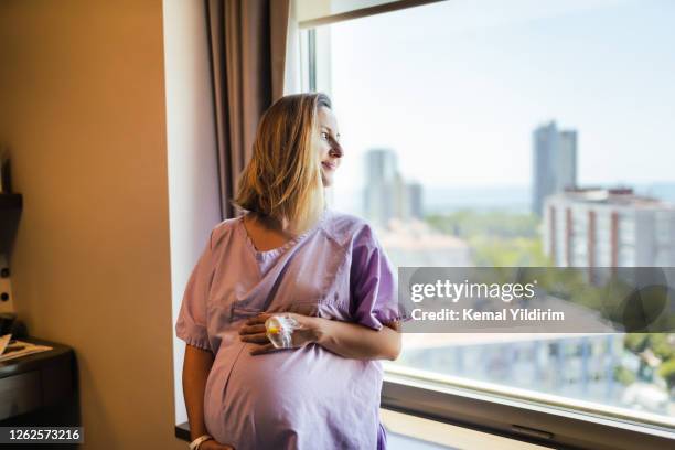 junge schwangere frau berührt magen, während warten travail in richtung fenster auf krankenhausstation - home birth stock-fotos und bilder