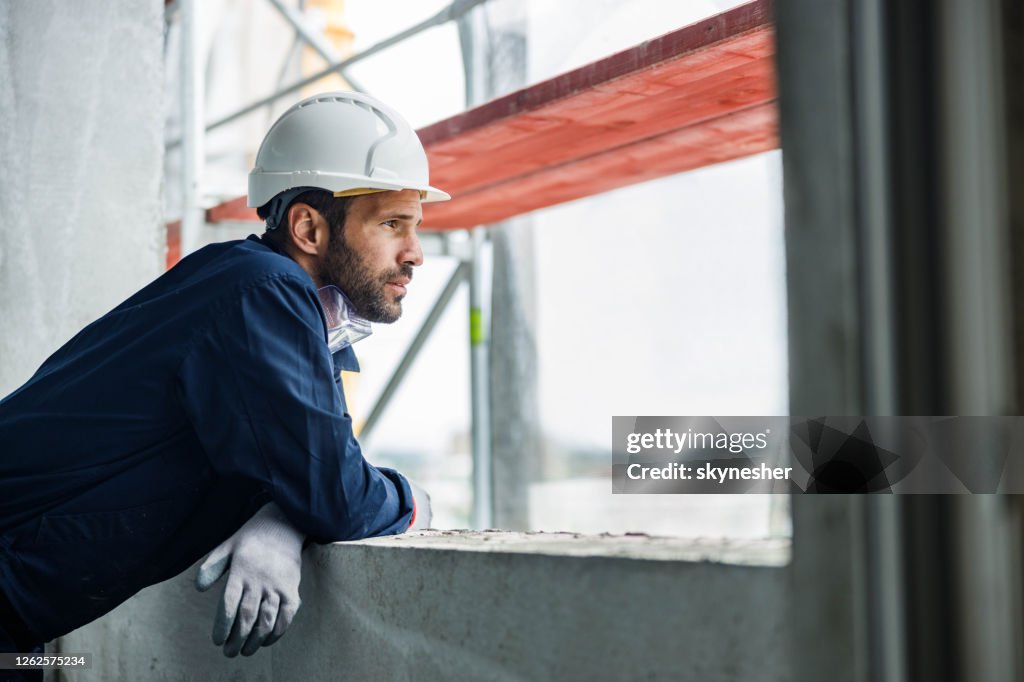 Pensive manual worker looking through window at construction site.