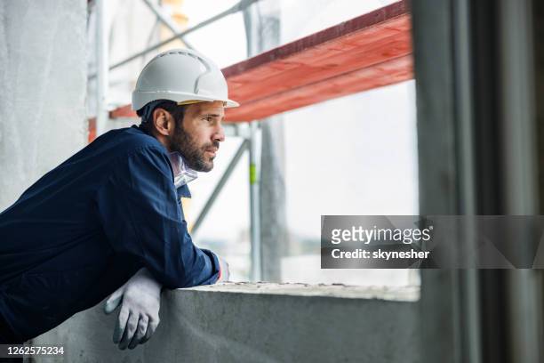 pensive manual worker looking through window at construction site. - building reflection stock pictures, royalty-free photos & images