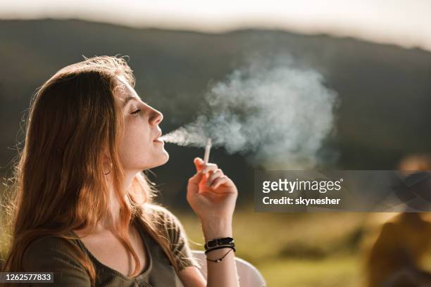 jonge roodharige vrouw die een sigaret in aard rookt. - rookkwestie stockfoto's en -beelden