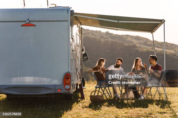 gelukkige vrienden die bij picknicklijst door de kampaanhangwagen in de zomerdag communiceren. - camper van stockfoto's en -beelden