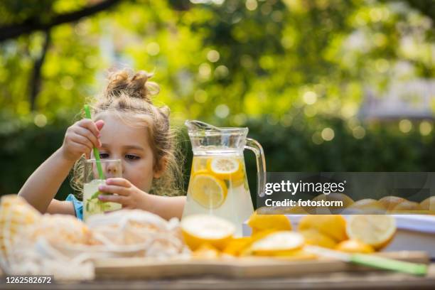 kleines mädchen nimmt eine hausgemachte limonade im heimischen hinterhof - lemonade stock-fotos und bilder