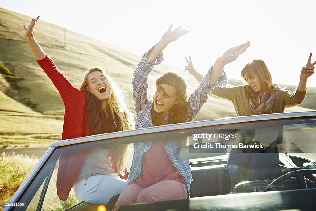 Women in parked convertible with arms in air