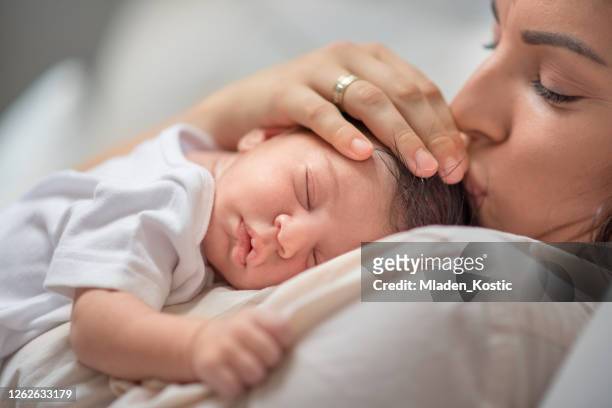 mother kissing newborn baby boy head while putting her child to sleep - mom resting stock pictures, royalty-free photos & images
