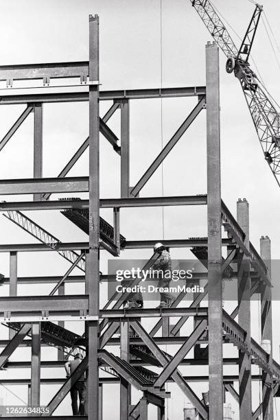 1970s Several Anonymous Silhouetted Men Construction Workers Assembling Steel I-Beam Framework For Multistory High-Rise Building