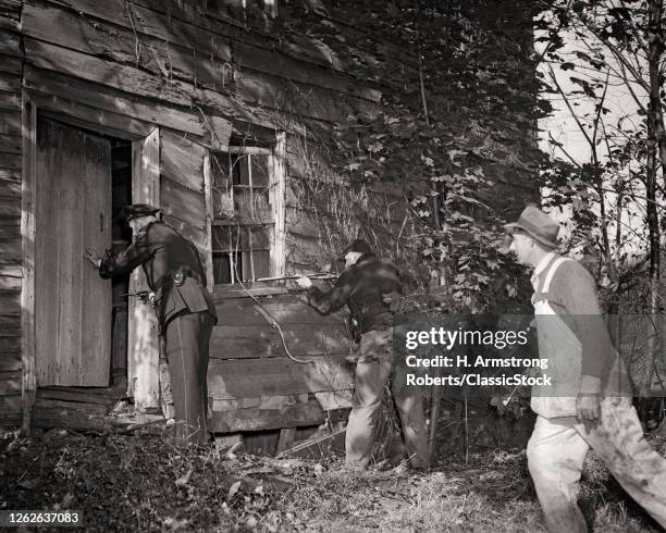 1940s Wary Uniformed Policeman And Posse Armed With Guns Approaching Abandoned Shack Searching For Escaping Crooks Hiding Inside