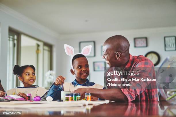 smiling father and his cute little children painting together at home - african easter stock pictures, royalty-free photos & images