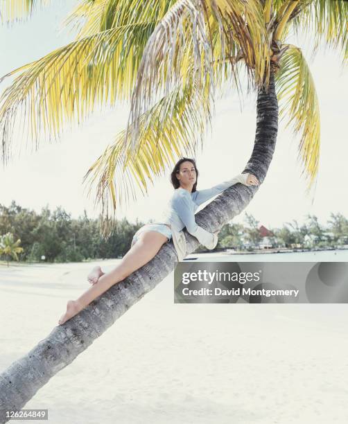 English socialite and columnist Tara Palmer-Tomkinson posing on a palm tree at a beach, 1998.