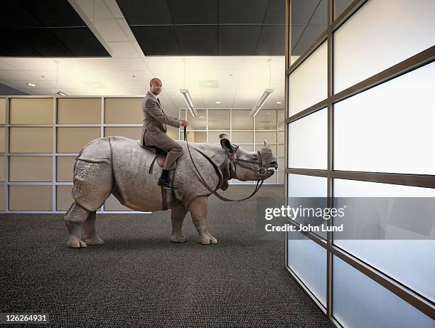 a businessman sits astride a rhinoceros in an offi - out of context foto e immagini stock