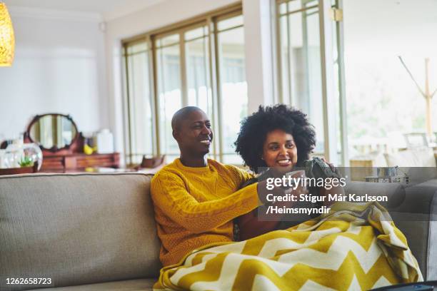 smiling couple sitting together at home and watching tv - african american watching tv stock pictures, royalty-free photos & images