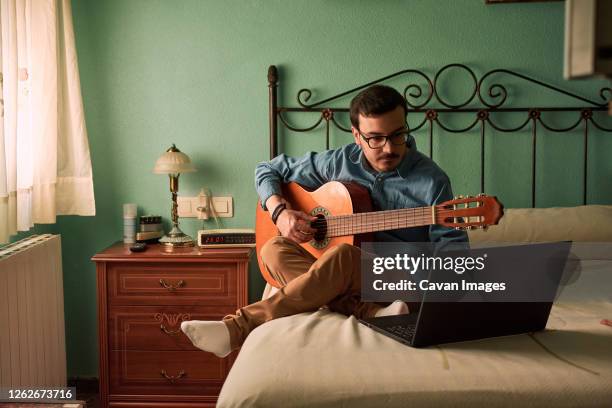 young man practices with the guitar by looking at his laptop at home - compositor fotografías e imágenes de stock