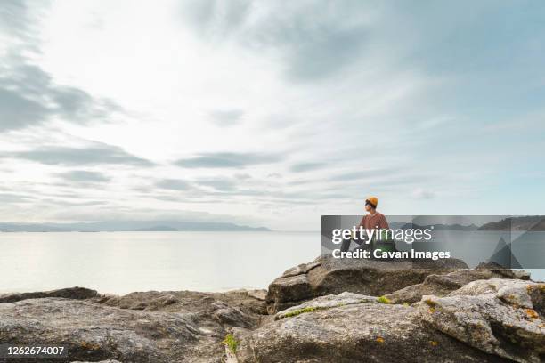 man exploring the coast sitting on the rocks - vigo - fotografias e filmes do acervo