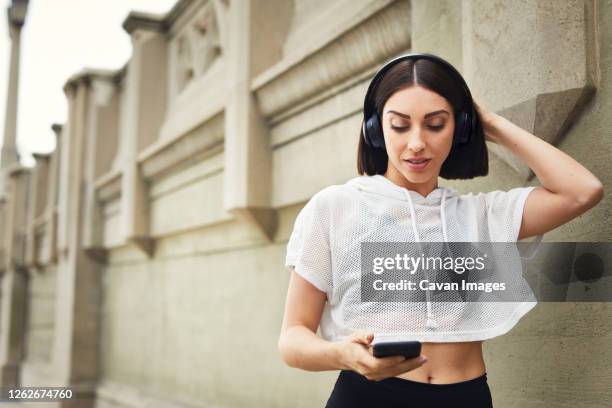 woman with headphones using smart phone by wall in city - headphone man on neck stock-fotos und bilder