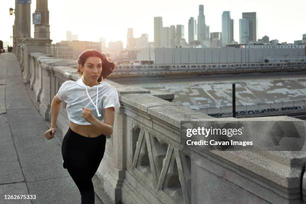 full length of jogger running on bridge while exercising in city - anzug ausland stock-fotos und bilder