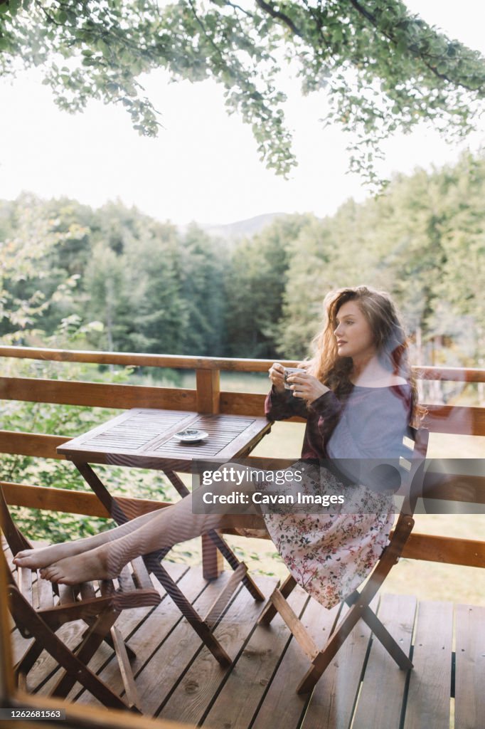 Young redhaid woman drinking coffee on tree house balcony