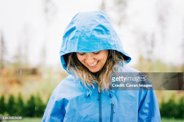 woman stood in the rain with a raincoat on smiling outside - raincoat stockfoto's en -beelden