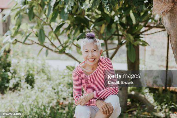 porträt der thailändischen hipster seniorin in ihrem garten - thai ethnicity stock-fotos und bilder