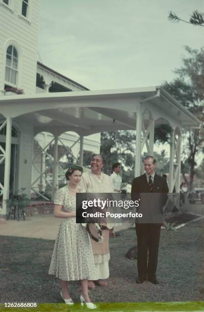 Queen Elizabeth II and Prince Philip, Duke of Edinburgh stand together with their host Queen Salote Tupou III in the grounds of the royal palace in...