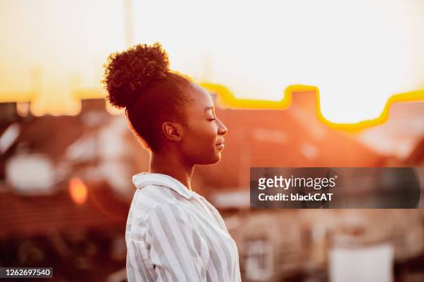 young african american woman is relaxing on the rooftop - bem estar mental imagens e fotografias de stock
