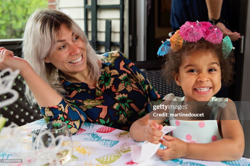 Mixed-race toddler playing at table outdoors with mother.