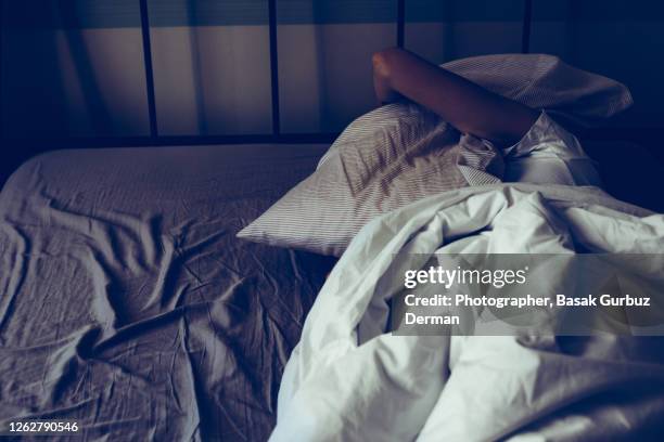 a woman trying to sleep more, having trouble sleeping due to noise, covering her ears with pillow ... - insonnia foto e immagini stock