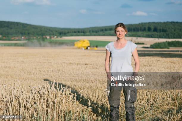 vrouwelijke landbouwer die zich op het tarwegebied bevindt, combineer harvester op de achtergrond - corporate portraits depth of field stockfoto's en -beelden