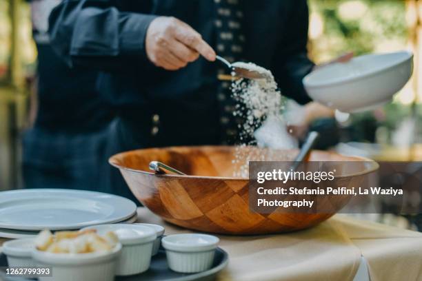 waiter's hand sprinkling parmesan cheese in bowl that contains food - sprinkles stock-fotos und bilder