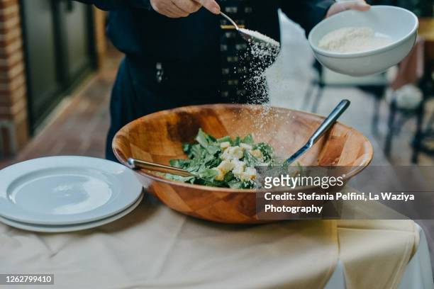 waiter's hands sprinkling parmesan cheese on cesar salad - strooisels stockfoto's en -beelden