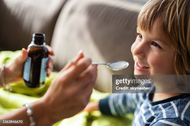 happy boy taking cough syrup from his parent at home. - syrup stock pictures, royalty-free photos & images