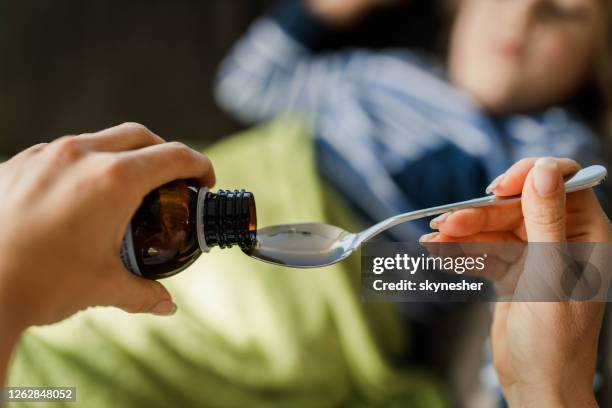 close up of unrecognizable mother pouring cough syrup into the spoon. - syrup stock pictures, royalty-free photos & images