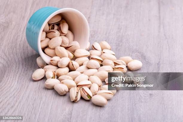 pistachio nuts in a white ceramic bowl on a wooden table. - pistachio stock pictures, royalty-free photos & images