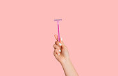 Young girl showing disposable razor on pink background, closeup of hand