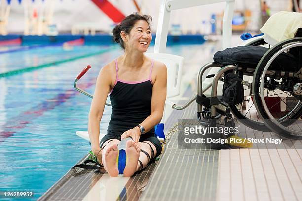 a paraplegic woman sits at the edge of a swimming pool on a lift beside her wheelchair and prepares to swim