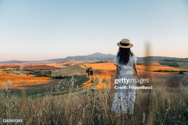 joven admirando la puesta de sol en un campo de trigo en toscana - tuscany fotografías e imágenes de stock