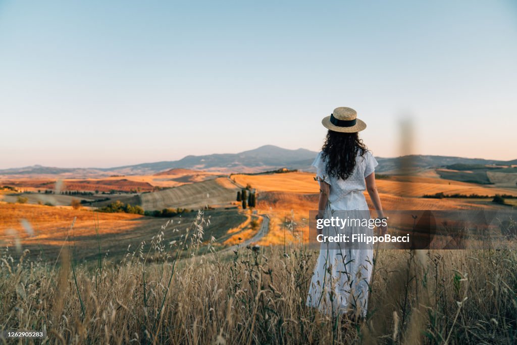 Young woman admiring sunset in a wheat field in Tuscany