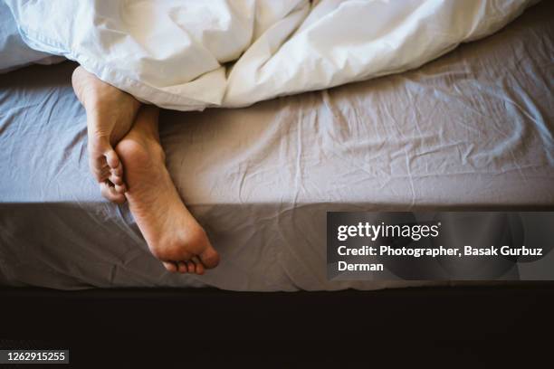 a woman's feet in bed under the blanket - duvet stock pictures, royalty-free photos & images