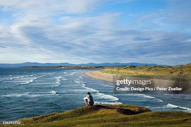 a person sitting at the water's edge at the beach near bundora - bundoran donegal stock pictures, royalty-free photos & images