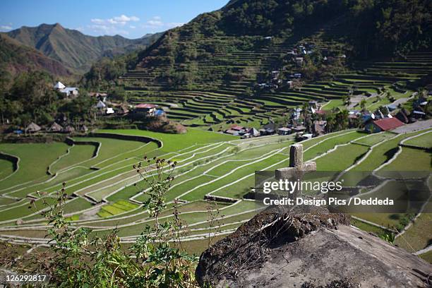 a cross sits on a ledge over the stunning ifugao stone-walled rice terraces surround the village of batad - cross religion stock-fotos und bilder