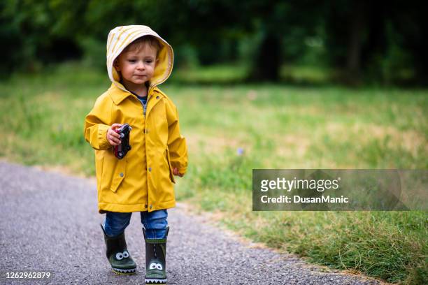 het spelen van de jongen in de regen, die laarzen en regenjas draagt - jongensbaby's stockfoto's en -beelden
